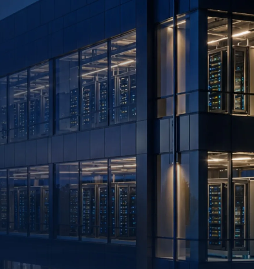 Server halls visible through the glass facade of a data center at night.