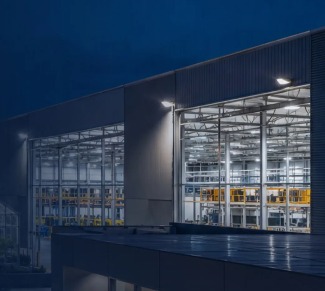 A large industrial building at night, its interior lighting visible through a glazed facade.